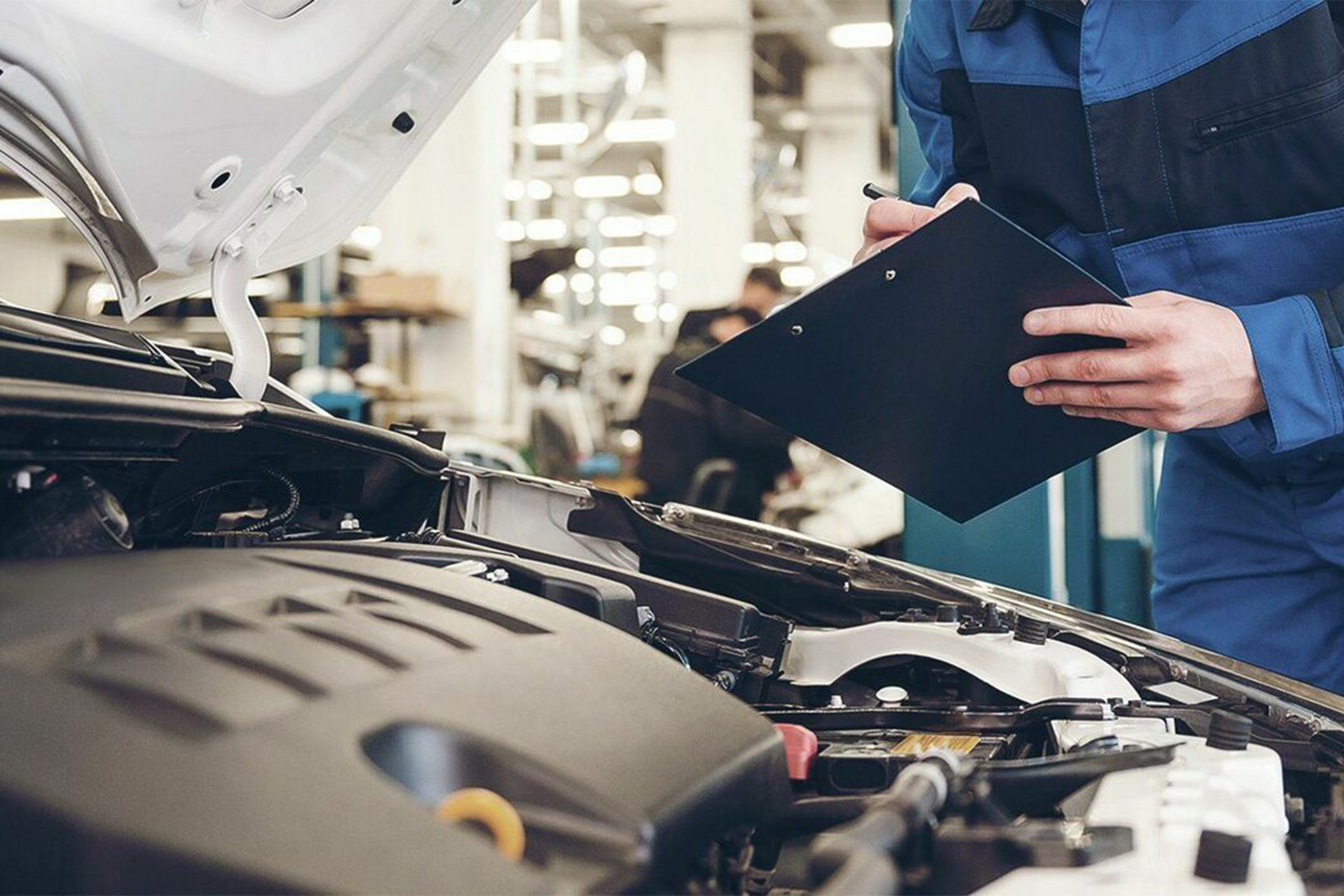 Car painter in protective clothes and mask painting automobile bumper with metallic paint and varnish in chamber workshop.