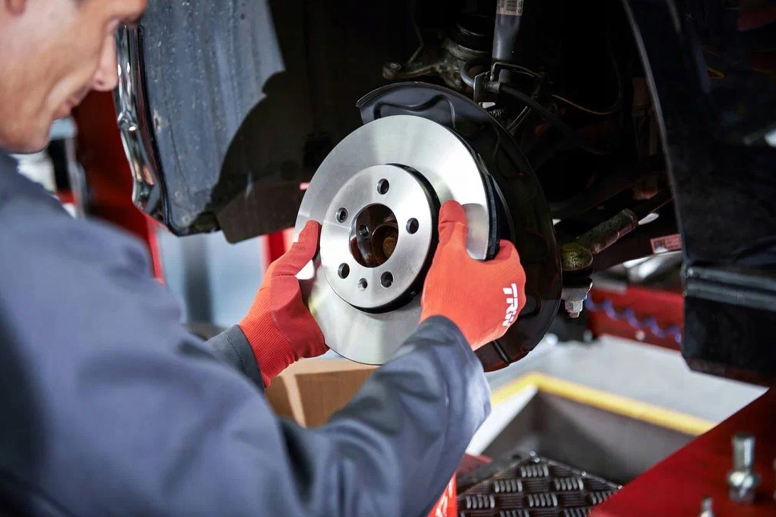 Car painter in protective clothes and mask painting automobile bumper with metallic paint and varnish in chamber workshop.