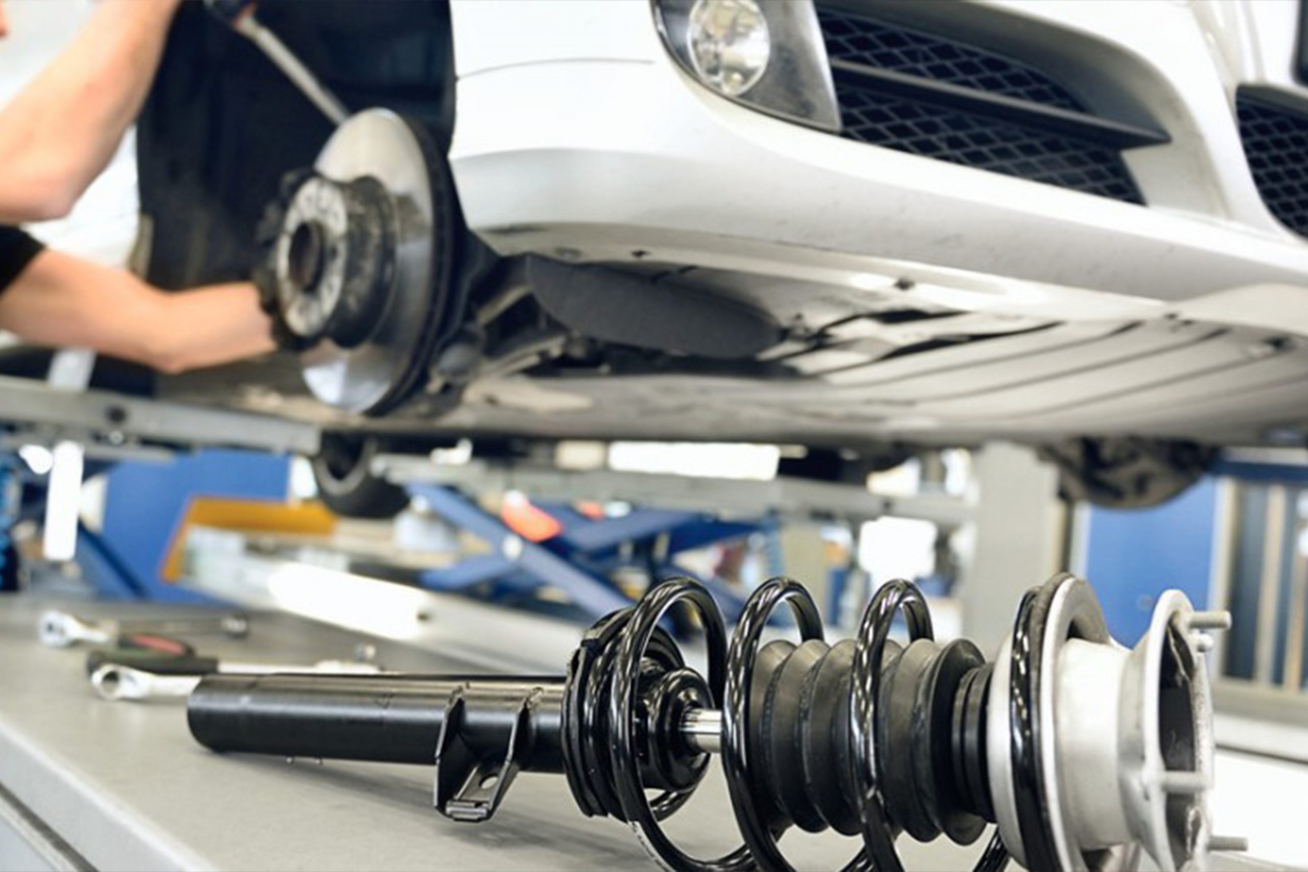 Car painter in protective clothes and mask painting automobile bumper with metallic paint and varnish in chamber workshop.
