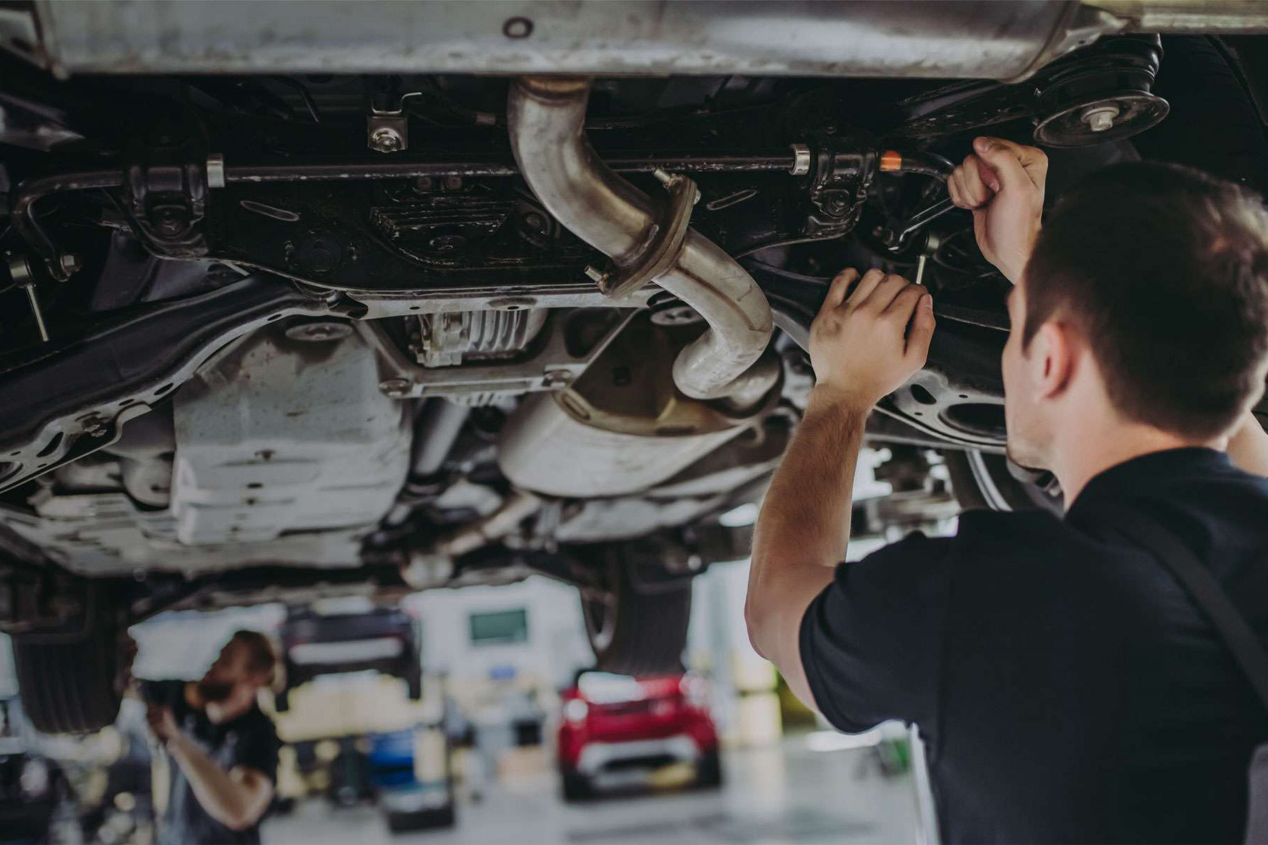 Car painter in protective clothes and mask painting automobile bumper with metallic paint and varnish in chamber workshop.