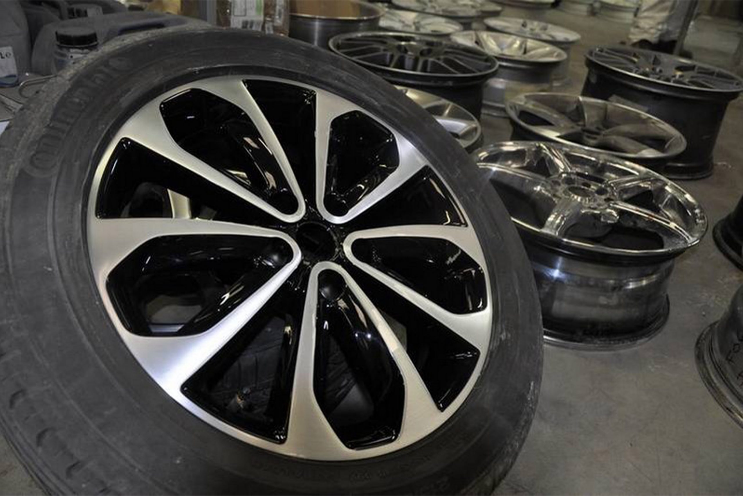 Car painter in protective clothes and mask painting automobile bumper with metallic paint and varnish in chamber workshop.