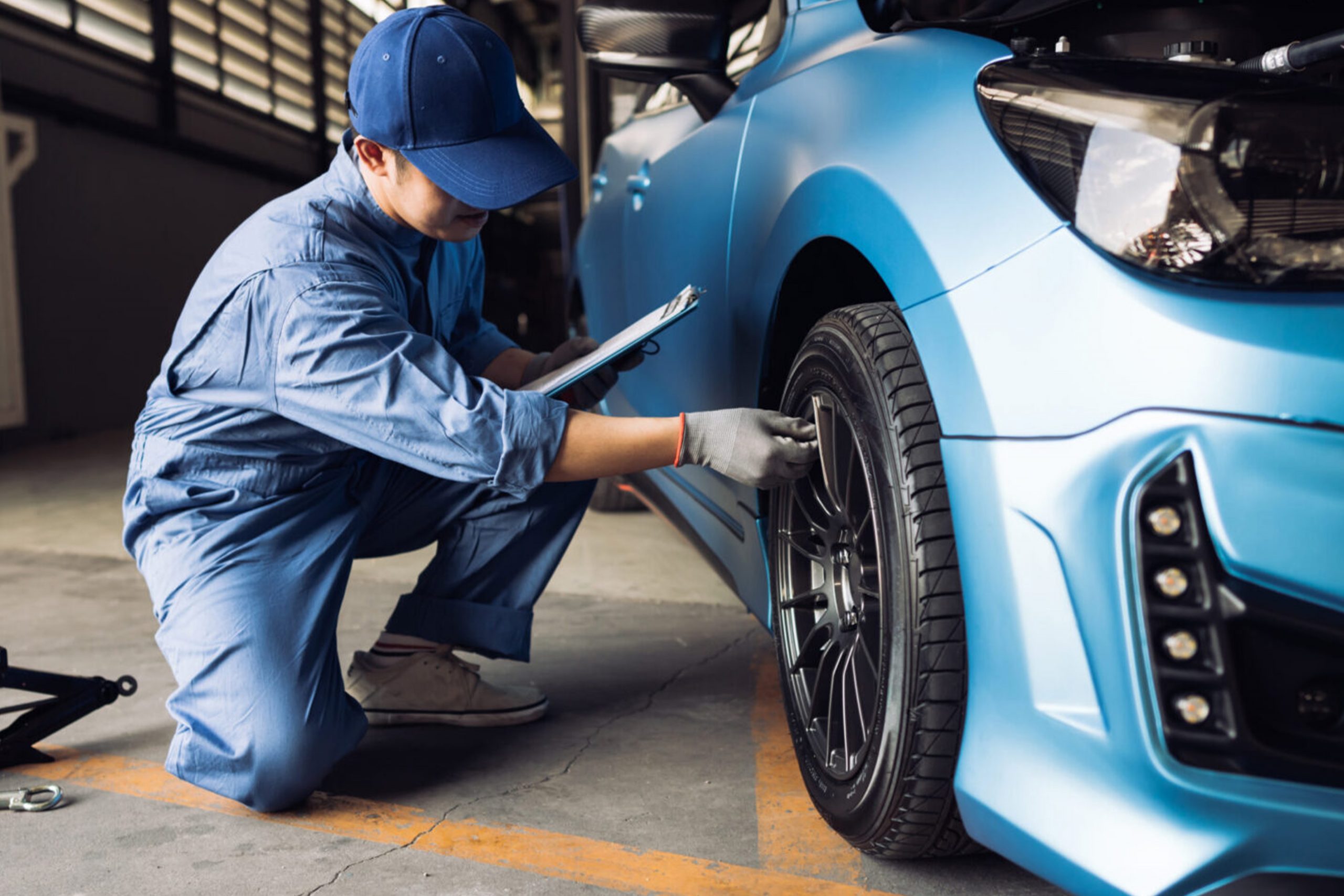Car painter in protective clothes and mask painting automobile bumper with metallic paint and varnish in chamber workshop.